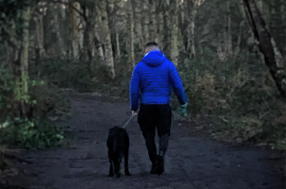 A dog and its trainer walking through woodland
